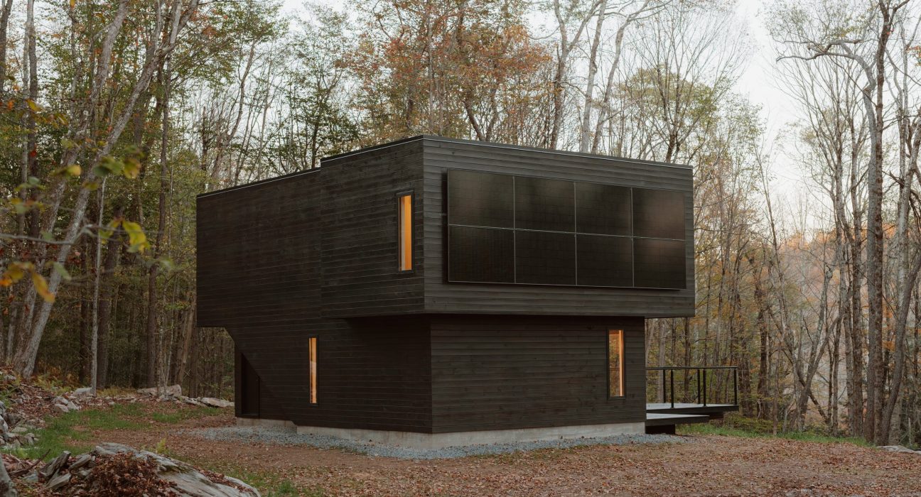 Exterior view of Forest Edge House with natural pine siding and an elevated platform extending over the forest slope.