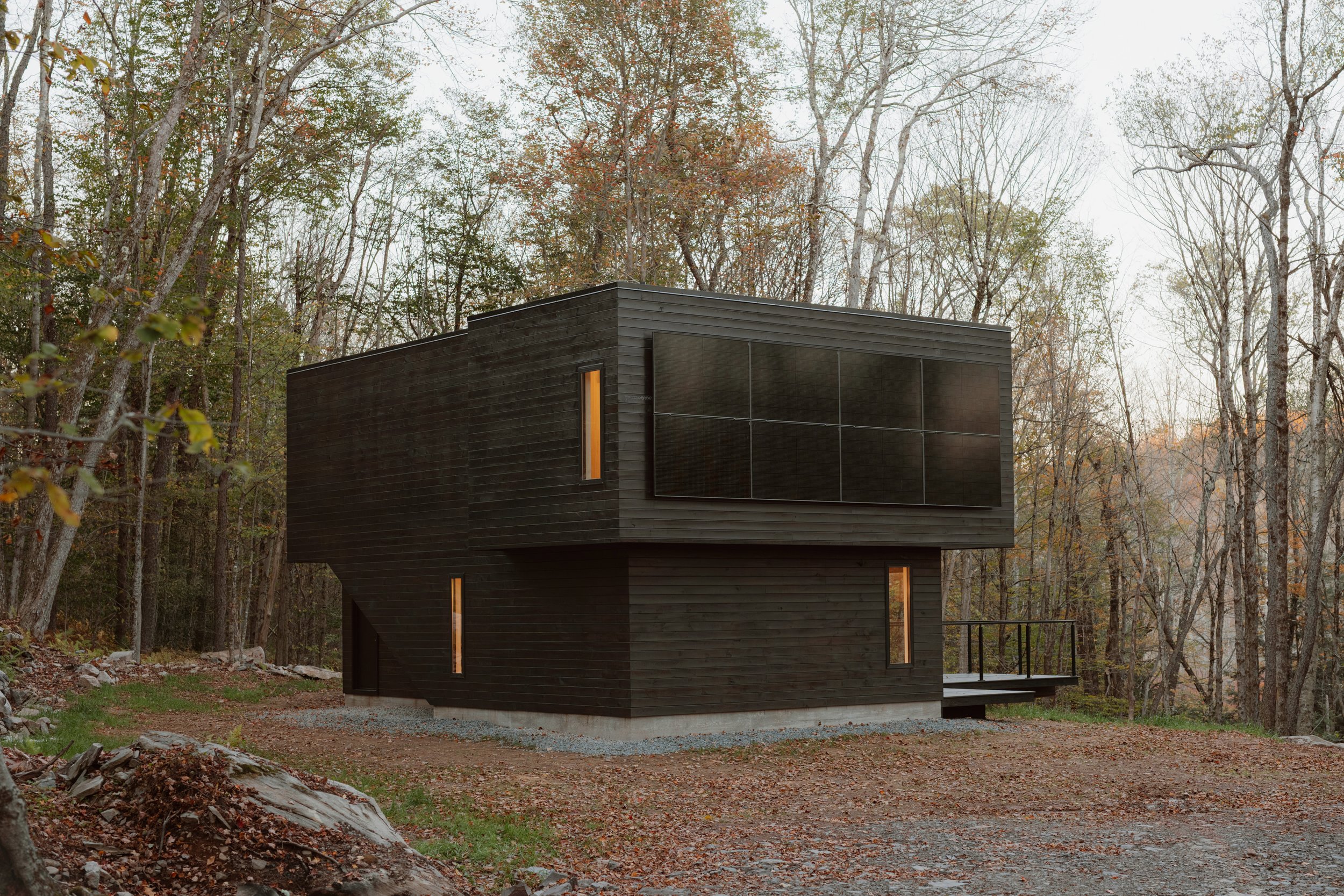 Exterior view of Forest Edge House with natural pine siding and an elevated platform extending over the forest slope.
