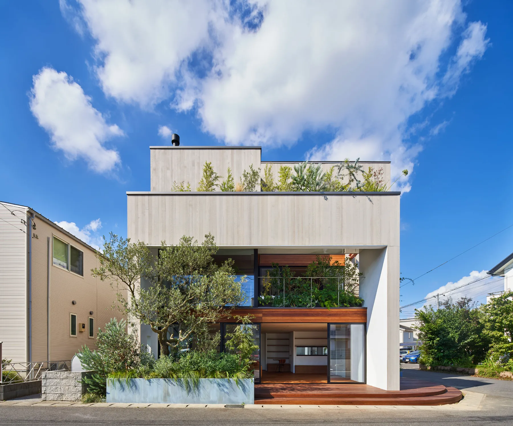 Exterior day view of House F by Kamakura Studio showing a two level structure with open sliding panels that connect the ground floor to the street and create a shared community space.